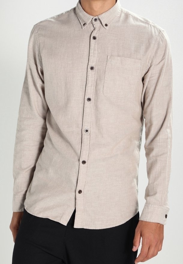 Beżowa koszula na długi rękaw zapinana na guziki, wykonana z lekkiego materiału, z kieszenią na piersi i ciemnymi guzikami jako akcentami.