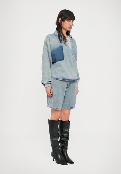 Τζιν τοπ με μια μεγάλη μπλε τσέπη, συνδυασμένο με τζιν σορτς. Μαύρες μπότες μέχρι το γόνατο με μυτερή μύτη συμπληρώνουν την εμφάνιση. Ανοιχτό ξέβαμμα, άνετη εφαρμογή.