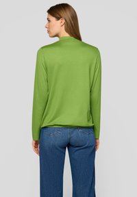 Grünes Langarmshirt mit glatter Textur, hohem Kragen und lockerer Passform, kombiniert mit blauen Jeans aus Denim mit Gesäßtaschen.