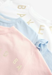 Tre T-shirt in rosa, blu e bianco. Ognuna presenta una scritta dorata che dice "BAKED." Il materiale è cotone morbido con una vestibilità regolare.