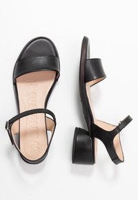 Musta nahkasaappaat, joissa on hihnasuunnittelu, matala lohkopohja ja avoin varvas. Sisäpuolella on sileä beige pohjallinen, jossa on brändin logo.