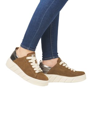 Brown suede sneakers with cream laces and a silver leather accent. Chunky white sole with vertical grooves. Worn with blue denim.