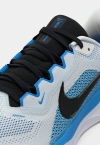 Nike sportcipő világoskék és fekete hálós felsőrésszel, amely kontrasztos kék részletekkel, fekete fűzőkkel és hangsúlyos fekete swoosh logóval rendelkezik.