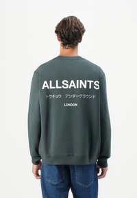 Sweatshirt verde escuro com mangas compridas, apresentando texto impresso em branco nas costas que inclui "ALLSAINTS" e "LONDRES". Corte casual.