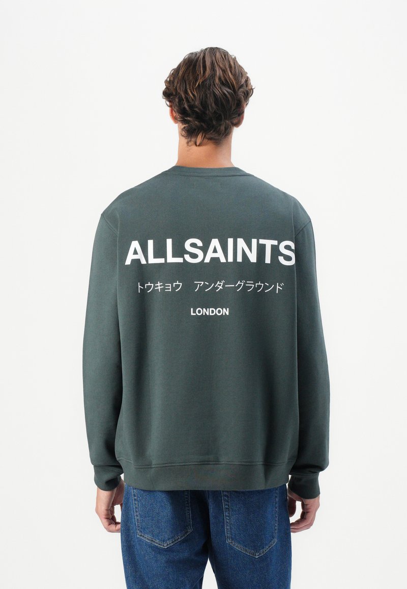 Sweatshirt verde escuro com mangas compridas, apresentando texto impresso em branco nas costas que inclui "ALLSAINTS" e "LONDRES". Corte casual.