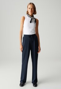 Witte mouwloze top, marineblauwe broek met koordsluiting, zwart-witte sjaal met patroon, gladde textuur, getailleerde pasvorm, gecombineerd met zwarte schoenen.