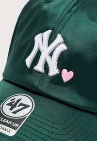 Πράσινο καπέλο μπέιζμπολ από λείο ύφασμα με λευκό κεντημένο λογότυπο "NY" και μια μικρή ροζ καρδιά. Περιλαμβάνει στρογγυλή ετικέτα με το εμπορικό σήμα.