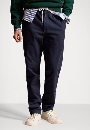 Pantalons de jogging en coton bleu marine avec taille élastique, cordon de serrage et poches latérales. Portés avec un sweat-shirt vert et une chemise à col à rayures en dessous.