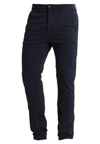 Lahkeet tummansinisiä puuvillachinoja suoran lahkeen muotoilulla, nappisuljenta ja etutaskut. Sileä pinta, minimaalinen saumaus ja kaareva helma.