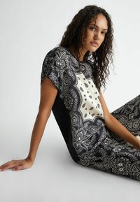 Top a motivi bianco e nero con maniche corte, caratterizzato da un pannello centrale color crema e intricati disegni paisley. Tessuto morbido.