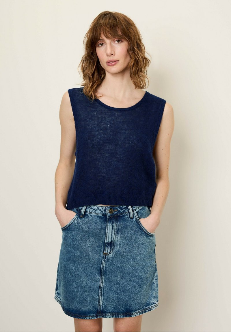 Granatowy bezrękawnik dzianinowy z okrągłym dekoltem, w połączeniu z jasnoniebieską spódnicą dżinsową z kieszeniami i zapięciem na guziki.
