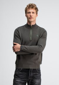 Dunkelgrüner Reißverschluss-Pullover mit hohem Kragen und gerippten Bündchen. Hat eine strukturierte Oberfläche und ein kleines Logo-Patch auf der Brust.