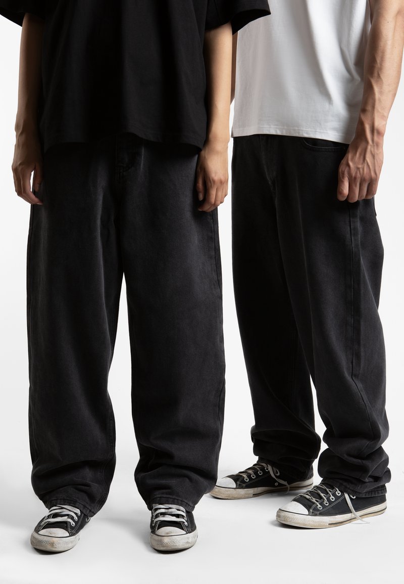 Black oversized denim pants, featuring a relaxed fit and a subtle texture. Paired with classic black and white sneakers.
