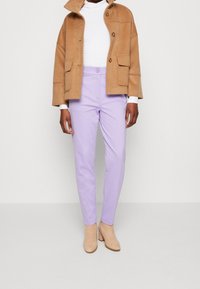 Bruine fleece jas met een kraag, witte coltrui, lilac op maat gemaakte broek en nude hakken. Bevat knoop- en zakdetails.