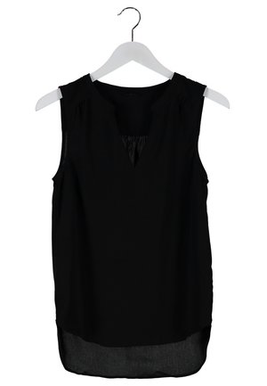 Vrouw draagt een mouwloos zwart topje en zwarte skinny broek met patroon, gecombineerd met zwarte en beige veterlaarsjes, staand tegen een effen achtergrond.