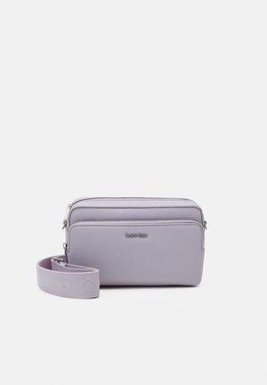 Sac bandoulière lilas en matériau synthétique lisse, doté d'une fermeture zippée, d'une bandoulière amovible et d'un logo de marque embossé à l'avant.