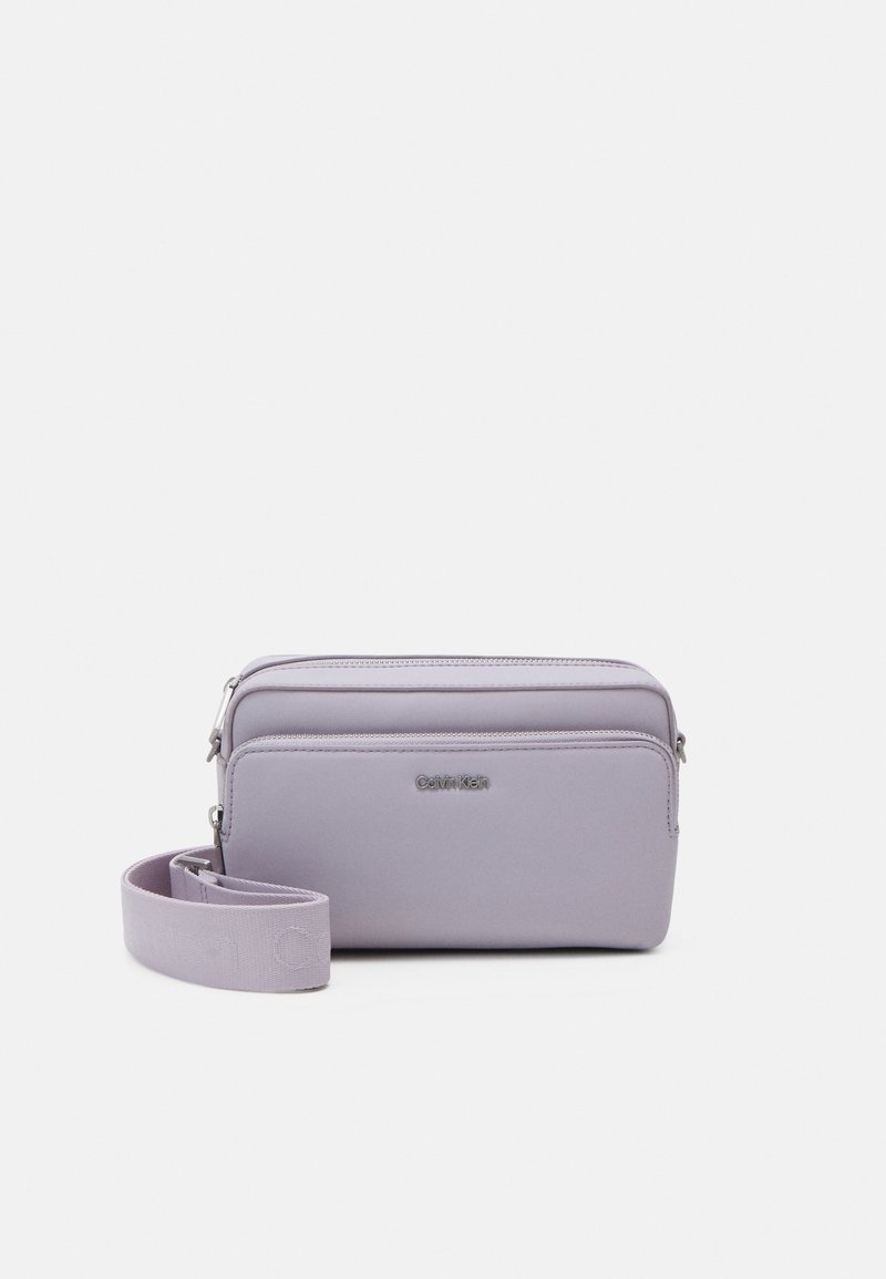 Lilac crossbody bag made of smooth synthetic material, featuring a zip closure, detachable strap, and embossed brand logo on the front.