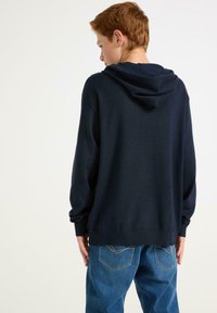 Felpa navy con vestibilità comoda e cappuccio regolabile con cordoncino, con polsini e orlo a costine. Abbinata a jeans di denim blu chiaro.