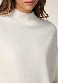Maglione a maglia beige chiaro con collo alto, caratterizzato da una sottile texture a pois e dettagli metallici su tutto il tessuto.