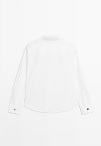 Witte lange mouwen shirt. Heeft een soepele textuur, klassieke kraag, afgeronde zoom en knoopmanchetten met contrasterende donkere knoopaccenten.