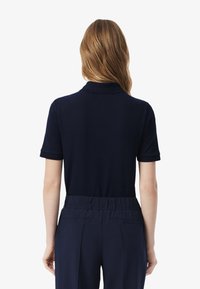 Granatowa koszulka polo z krótkim rękawem z miękkiego materiału, z kołnierzykiem i ściągaczami na rękawach, w połączeniu z granatowymi spodniami na gumce, minimalistyczny design.