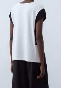 Kortärmad topp med vit front och svart baksidan. Tillverkad av ett mjukt tyg med lös passform, något längre bak.