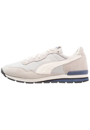 Niskie trampki Puma w kolorze beżowym i białym z panelami ze skóry zamszowej i tkaniny, białym paskiem Puma, niebieskim akcentem na pięcie i czarną podeszwą.