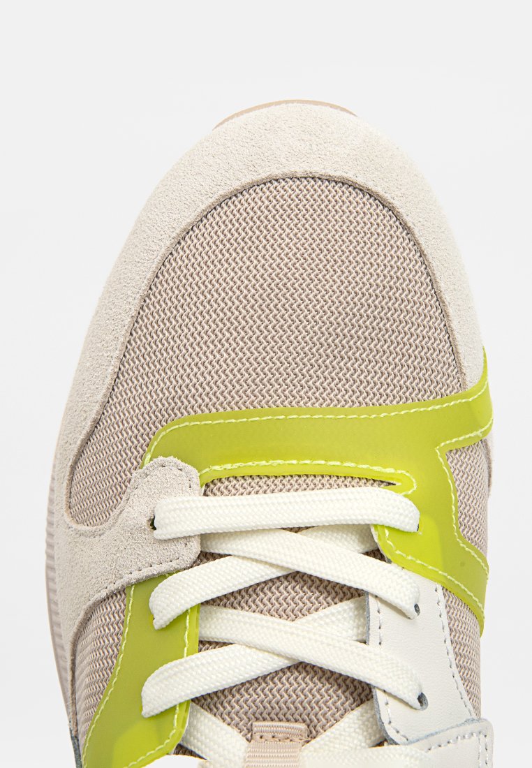 Baskets beiges avec une tige en mesh textile et en daim. Accents synthétiques verts et lacets blancs. Bout arrondi et semelle cushioned.