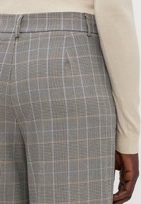 Pantaloni grigi a quadri con motivo houndstooth, caratterizzati da sottili dettagli color tan e una vestibilità su misura, con vita visibile e tasche laterali.