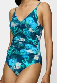 Eénstuk zwempak in een donker teal met een blauw en wit bloemenpatroon. Kenmerkt zich door geplooide details en dunne schouderbandjes. Gouden accent aanwezig.