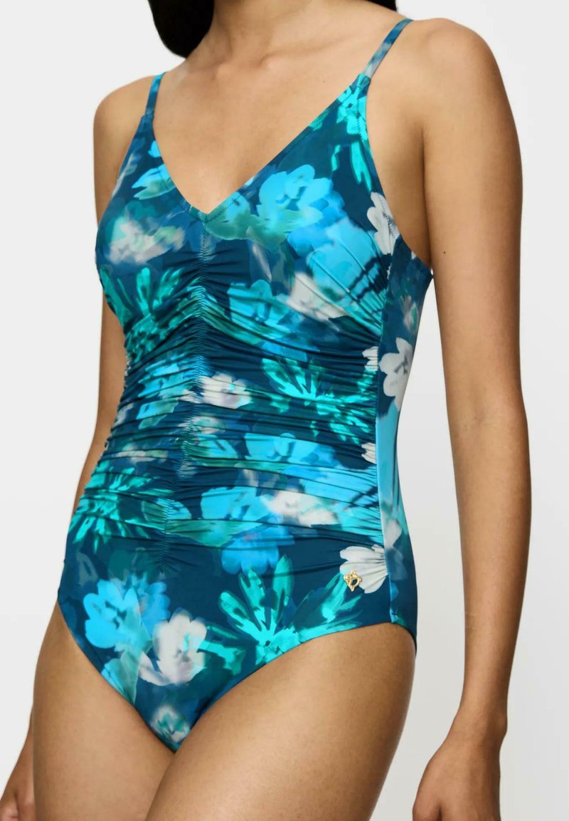 Eénstuk zwempak in een donker teal met een blauw en wit bloemenpatroon. Kenmerkt zich door geplooide details en dunne schouderbandjes. Gouden accent aanwezig.