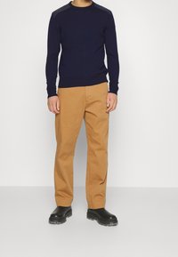 Námořnicky modrý svetr s dlouhým rukávem a raglánovým střihem ramen, doplněný o béžové kalhoty rovného střihu a černé boty s gumovou podrážkou. Celkově hladká textura.