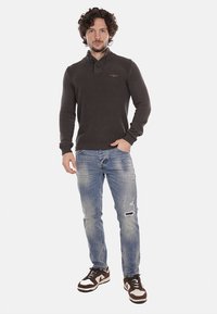 Maglione a coste grigio scuro con colletto e dettagli a bottoni; jeans chiari strappati blu; sneaker bianche e marroni con un design audace.