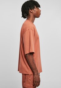 Tricou cu mânecă scurtă de culoare ruginiu. Prezintă o croială lejeră, material din bumbac moale și detalii cusute la guler și mâneci.