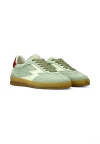 Sneaker in camoscio verde chiaro con lacci verde oliva, dettagli crema e un tacco rosso. Presenta una suola in gomma e un design perforato.