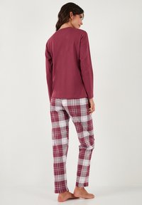 Hosszú ujjú bordó felső és kockás pizsamanadrágok, melyek bordó, fehér és fekete árnyalataiban pompáznak, sima textúrájúak és testhezálló kialakításúak.