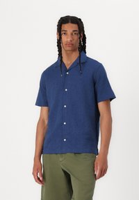 Short-sleeve navy shirt in textured fabric with a notched collar and five white buttons. Paired with olive green shorts.