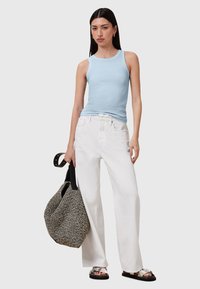 Světle modrý top bez rukávů v kombinaci s bílými širokými kalhotami. Černobílá vzorovaná taška, stříbrné sandály s tlustým páskem.