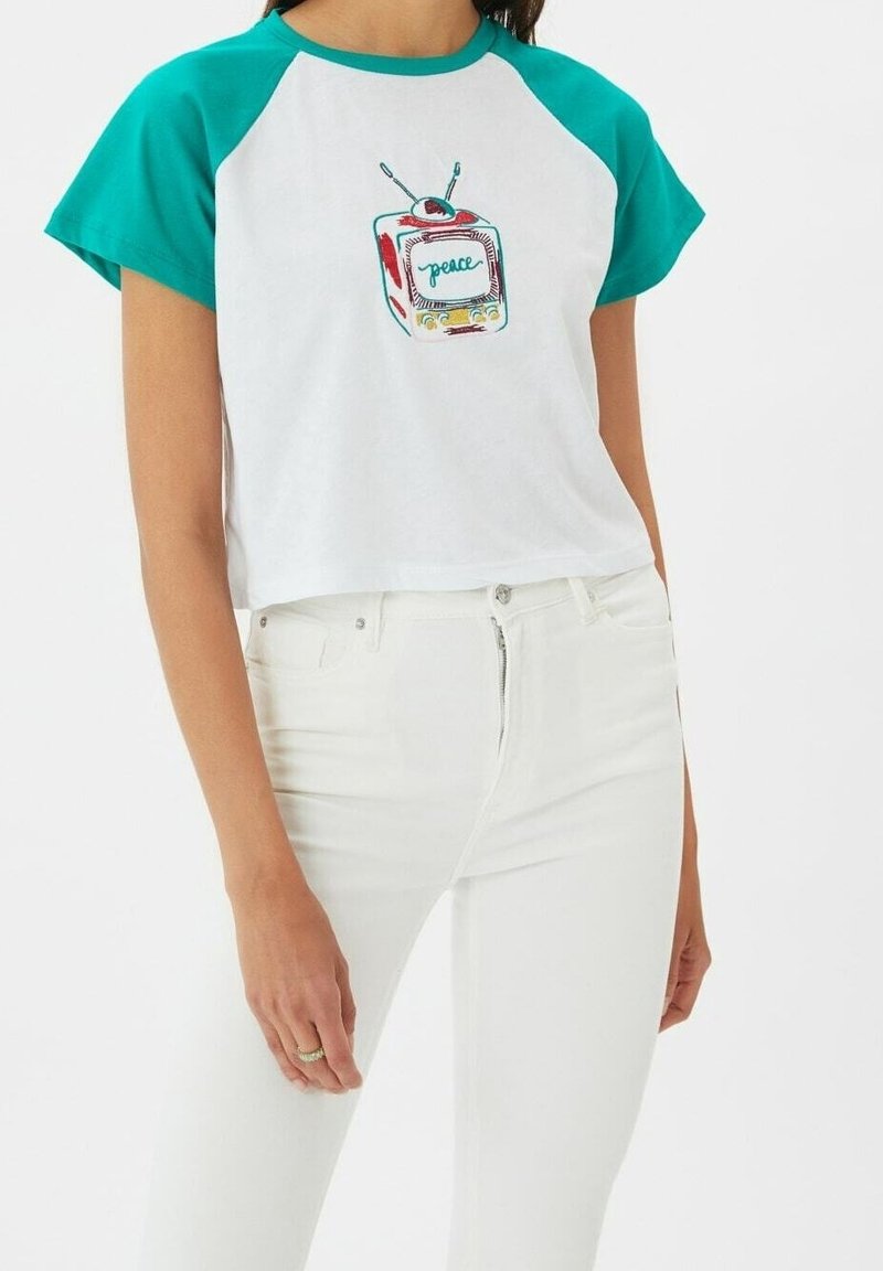 Bílý zkrácený tričko s tyrkysovými raglánovými rukávy. Na přední straně se nachází barevná retro grafika televizoru s nápisem "peace" uprostřed. Bavlněný materiál.