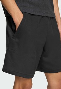 Pantaloni shorts neri a trama con tasche laterali, caratterizzati da una vestibilità comoda e una cintura elastica. La superficie presenta un motivo intrecciato distintivo.