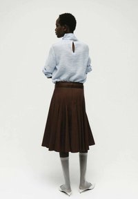 Camicia azzurra chiara a maniche lunghe con dettaglio a buco chiave sulla schiena, abbinata a una gonna marrone svasata. Calze grigie al ginocchio e scarpe bianche completano l'outfit.