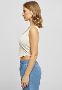 Krēmkrāsas cropped top ar šaurām siksnām, apvienots ar gaiši zilām džinsu šortiem ar elastīgu jostu un sānu šķēlumu.