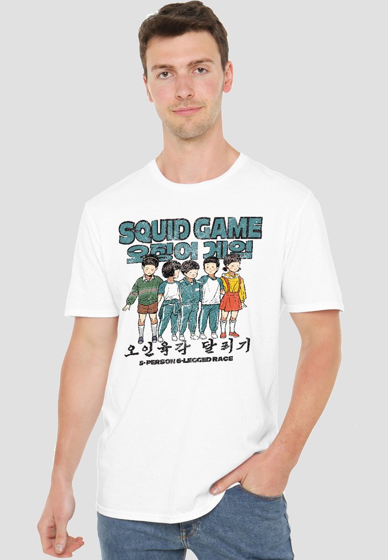 Man wearing a white t-shirt featuring a graphic of characters from "Squid Game" in a six-legged race, with Korean text below the design.