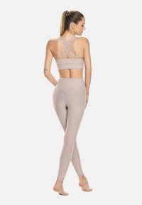 Svetlo bež športni modrček z križnimi naramnicami na hrbtu, v kombinaciji z visokim pasom legice v usklajeni barvi, ki se ponašajo z gladko teksturo in oblikovalskimi šivi.