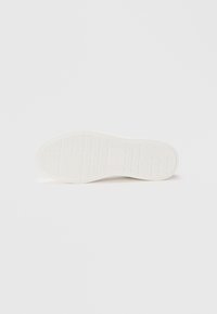 White rubber sneaker sole with textured grip patterns, featuring a smooth finish and a rounded shape. No visible branding or accents.