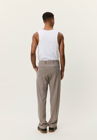 Ελαφρύ λευκό μπλουζάκι χωρίς μανίκια και μπεζ παντελόνι με ριγέ λεπτομέρειες, με εφαρμοστή γραμμή, πίσω τσέπες και μαύρα παπούτσια.