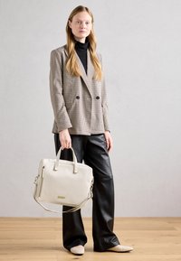 Blazer beige à carreaux double boutonnage, col roulé noir, pantalon en cuir noir à jambes larges, tenant un sac structuré couleur crème avec une sangle amovible.