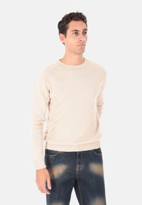 Maglione beige lavorato a maglia con scollatura rotonda e polsini a coste. Abbinato a jeans in denim scuro con effetto sbiadito e cuciture visibili.