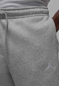 Grå fleece joggingbukser med elastisk talje og snor. Har et lille broderet logo på den nedre del af benet. Blød tekstur.