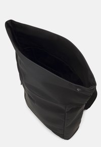 Zaino nero a chiusura con bottone a pressione, aperto largamente per mostrare l'interno spazioso vuoto.